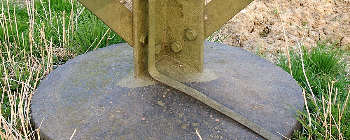 Galvanized steel transmission tower leg bolted to a concrete foundation, with a flat earthing strip running down the leg into the ground